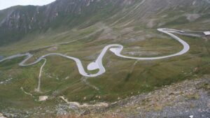 Route de montagne en lacets sur un versant d'herbe rase, avec quelques voitures sur la chaussée
