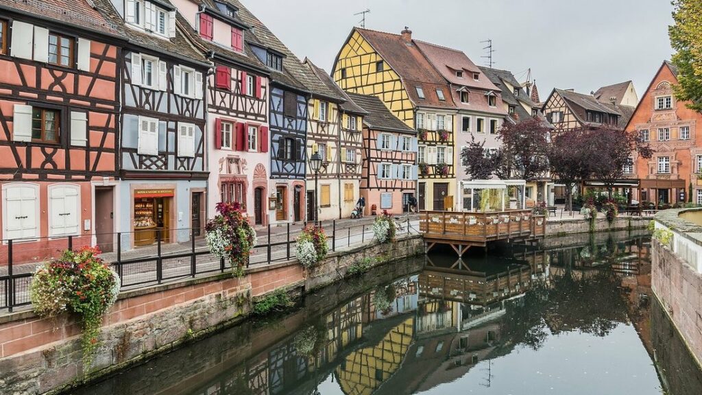 Canal bordé de maisons à colombages colorées et de jardinières fleuries, avec leurs reflets dans l'eau
