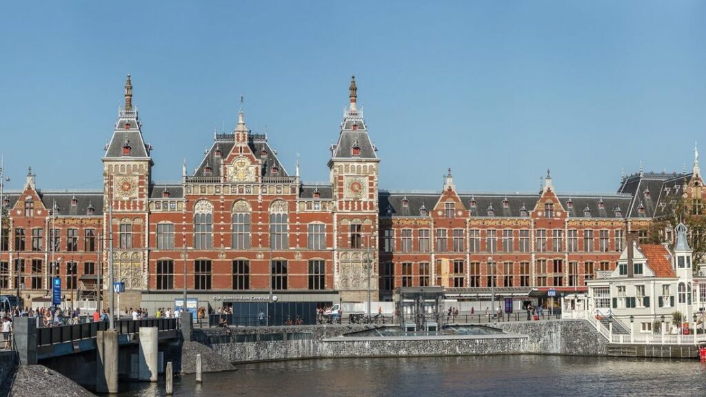Façade de brique rouge de la gare centrale d'Amsterdam, deux tours à horloge, vue depuis l'autre côté de l'eau