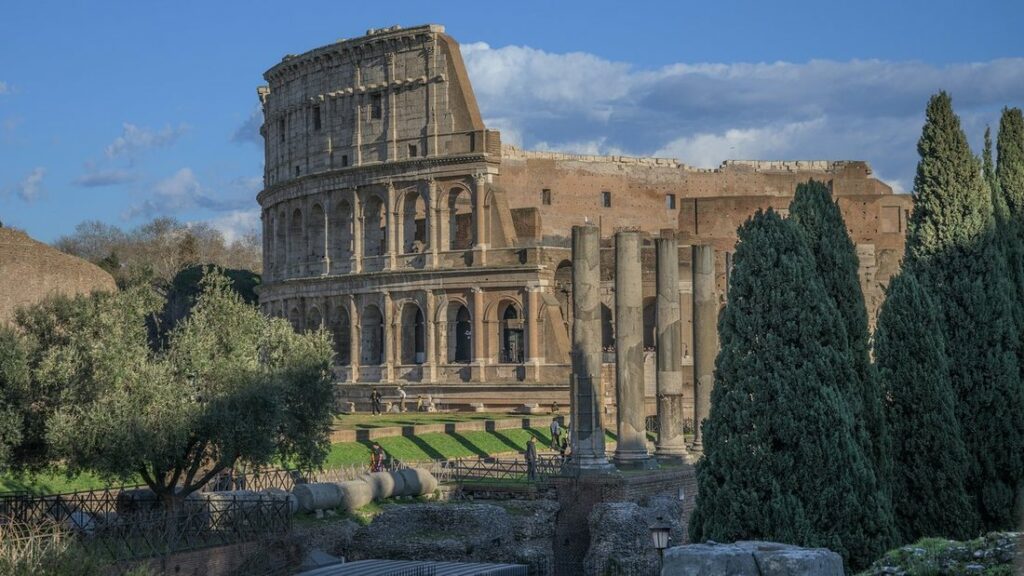 Le Colisée vu depuis le Forum romain, derrière des colonnes antiques et des cyprès, avec quelques visiteurs au pied