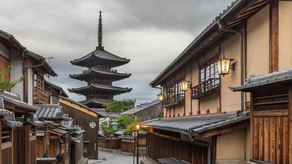 Ruelle pavée de Kyoto bordée de maisons en bois aux lanternes allumées, avec une pagode à cinq étages au fond