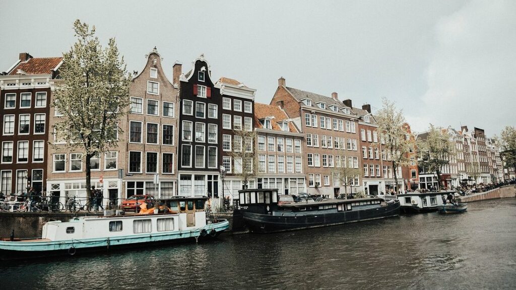 Maisons de brique à pignons étroits le long d'un canal d'Amsterdam, avec des péniches amarrées et des arbres