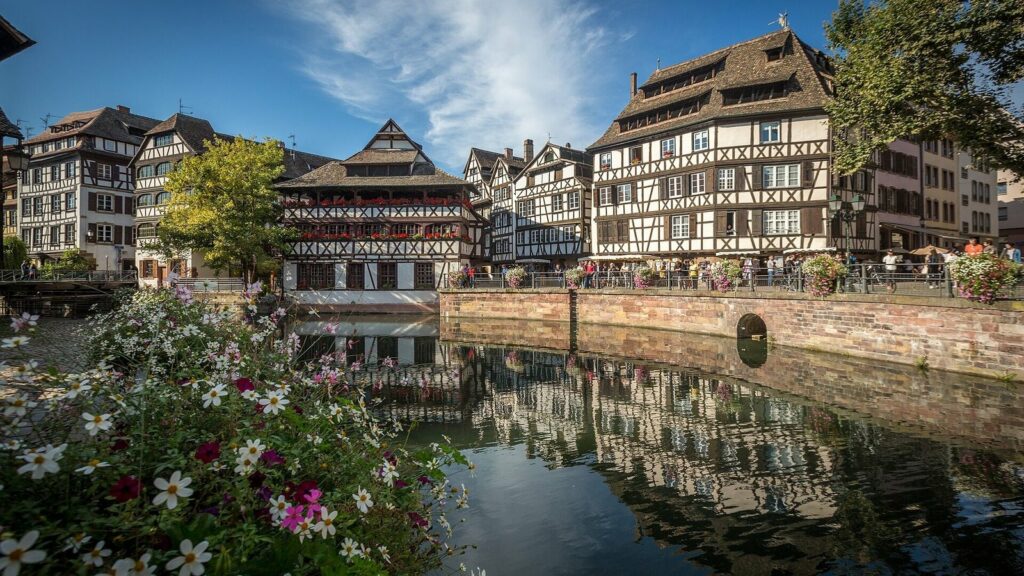 Maisons à pans de bois de la Petite France à Strasbourg, reflétées dans un canal bordé de fleurs