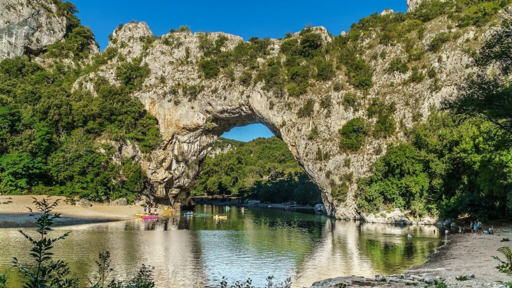 Le Pont d'Arc, arche de calcaire au-dessus de la rivière Ardèche, avec des canoës près de la plage