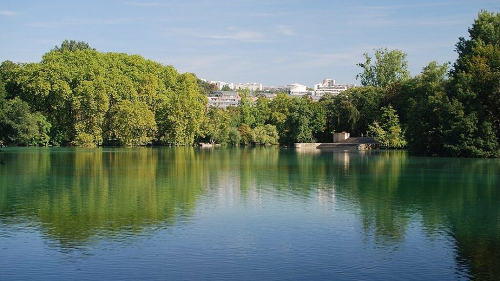 Lac du parc de la Tête d'Or à Lyon, eau calme et verte bordée d'arbres, immeubles lointains