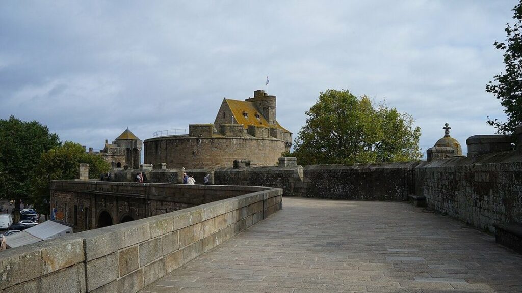 Chemin de ronde dallé des remparts de Saint-Malo, avec la tour du château au fond et un ciel couvert