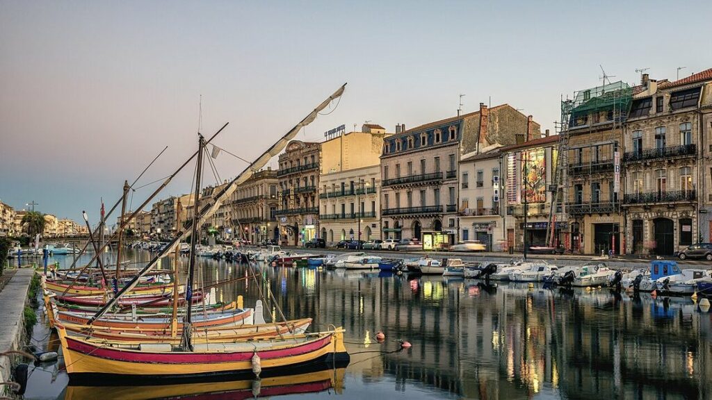Barques colorées à coque jaune amarrées dans un canal de Sète, face à des immeubles anciens et leurs reflets