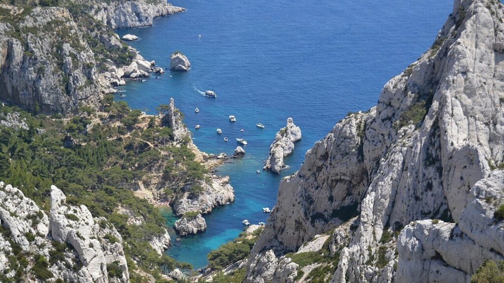 Calanque de Sugiton vue d'en haut : eau bleue profonde entre des parois de calcaire blanc, petits bateaux