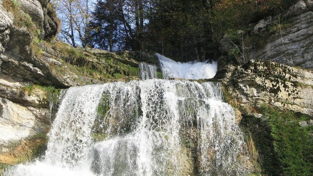 Cascade du Hérisson, nappe d'eau blanche qui dévale des roches calcaires sous les arbres