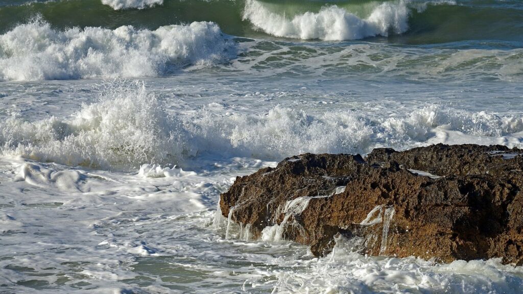Vagues qui se brisent en gerbes d'écume sur un rocher brun, mer vert sombre, côte près de La Canée en Crète