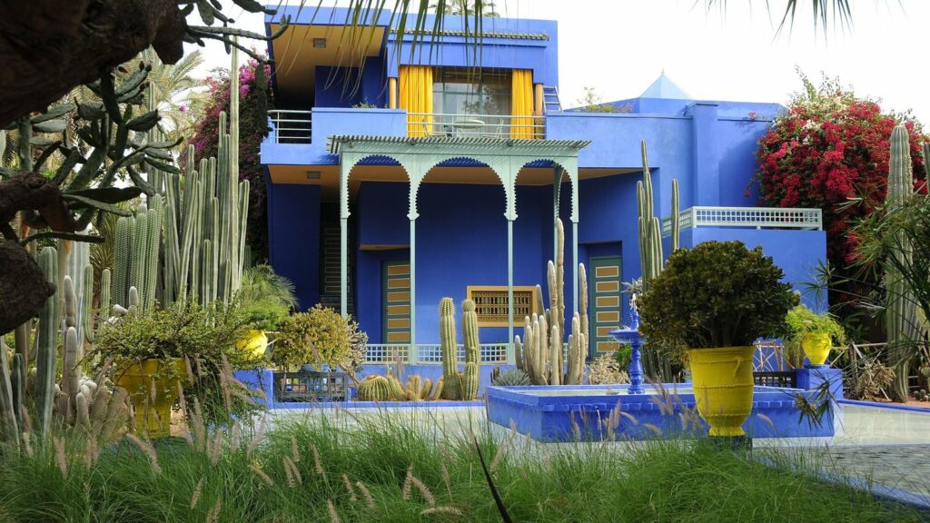 Villa bleu électrique du jardin Majorelle à Marrakech, entourée de cactus, de palmiers et de pots jaunes, devant un bassin