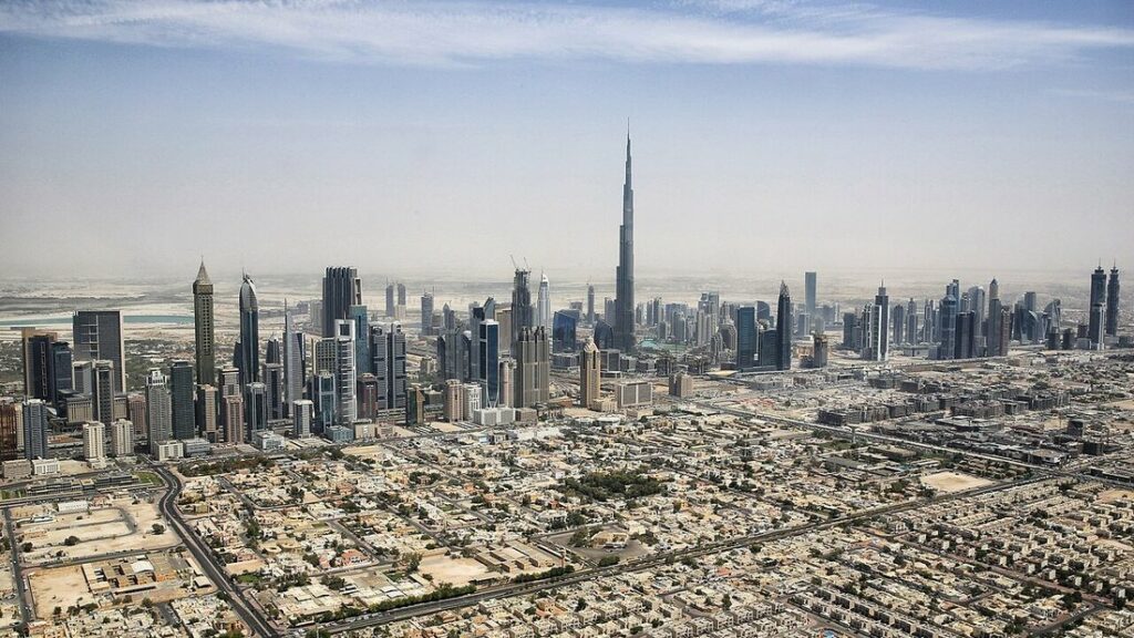 Vue aérienne de gratte-ciel dominés par la Burj Khalifa, au-dessus de quartiers de maisons basses, sous un ciel voilé