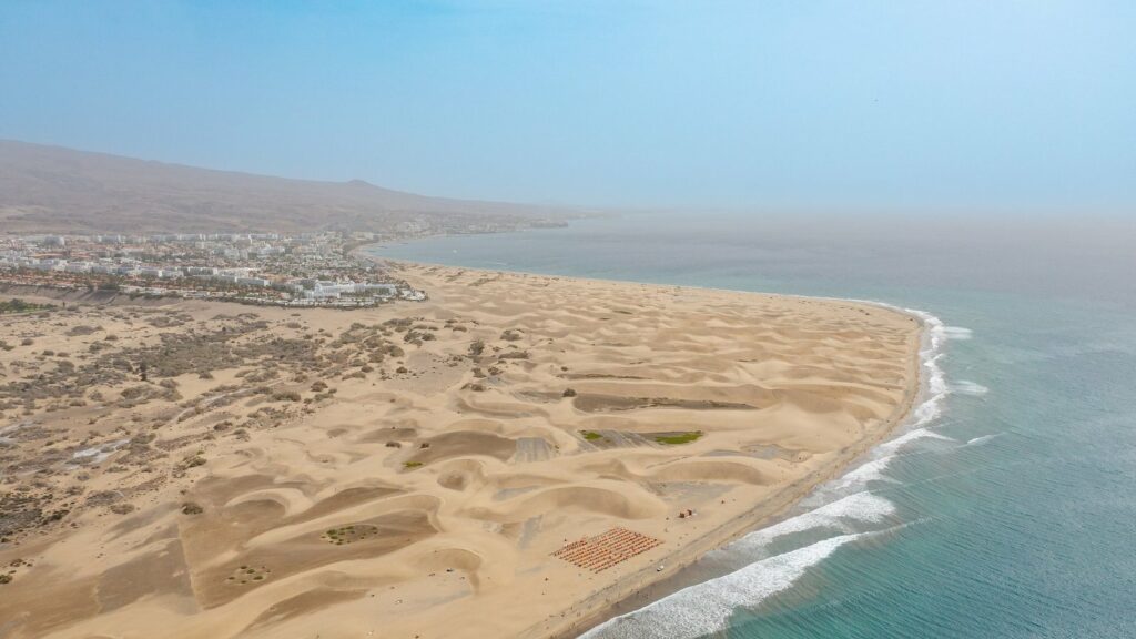 Vue aérienne des dunes de Maspalomas à Grande Canarie : une langue de sable devant une station balnéaire, avec l'océan sur la droite