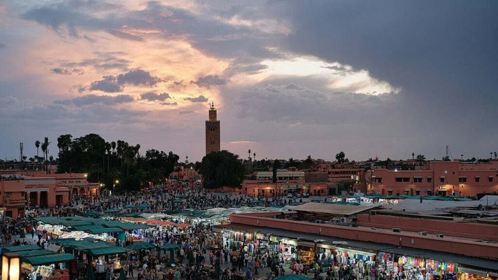 Place Jemaa el-Fna à Marrakech au crépuscule, avec ses étals éclairés, la foule et un minaret dans le fond