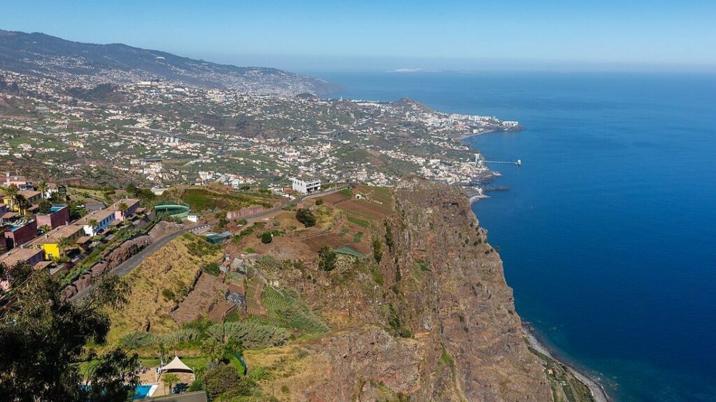 Vue plongeante sur la côte de Madère depuis une falaise, avec des villages en terrasses et l'océan bleu