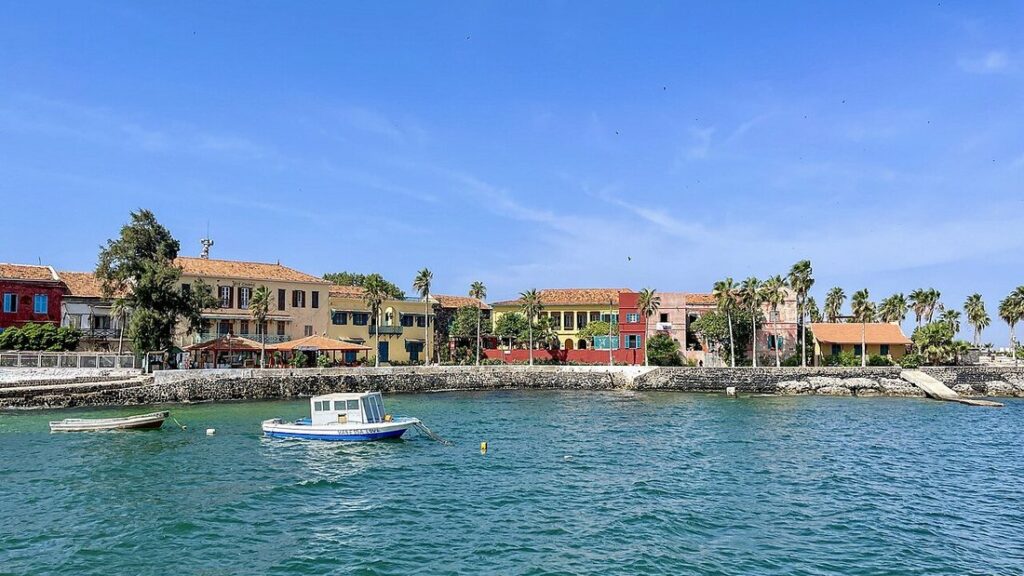 Façades colorées et palmiers au bord d'une petite baie, avec un bateau blanc et bleu sur une eau verte