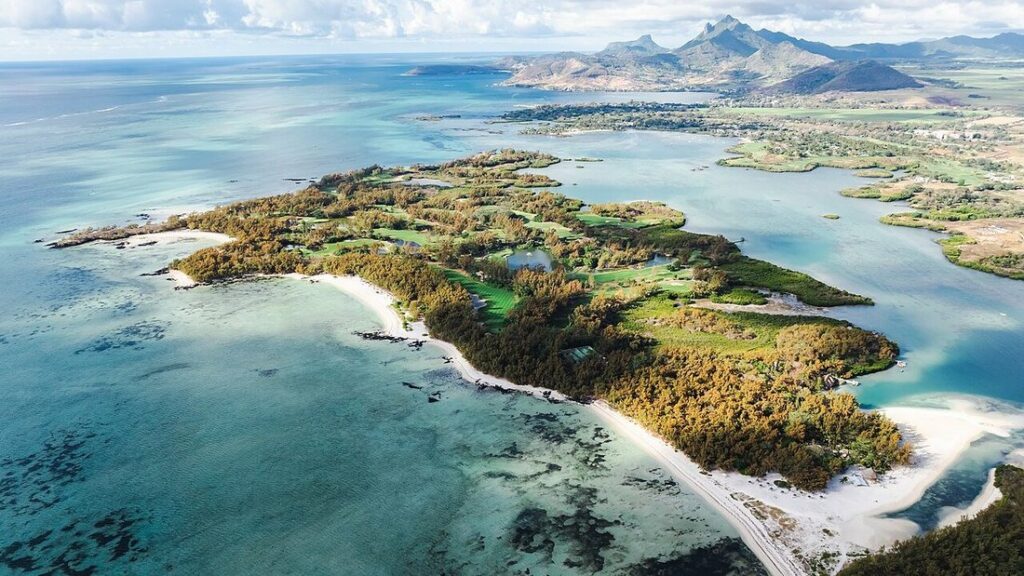 Vue aérienne d'une île boisée bordée de sable blanc, d'un lagon turquoise et de montagnes au loin