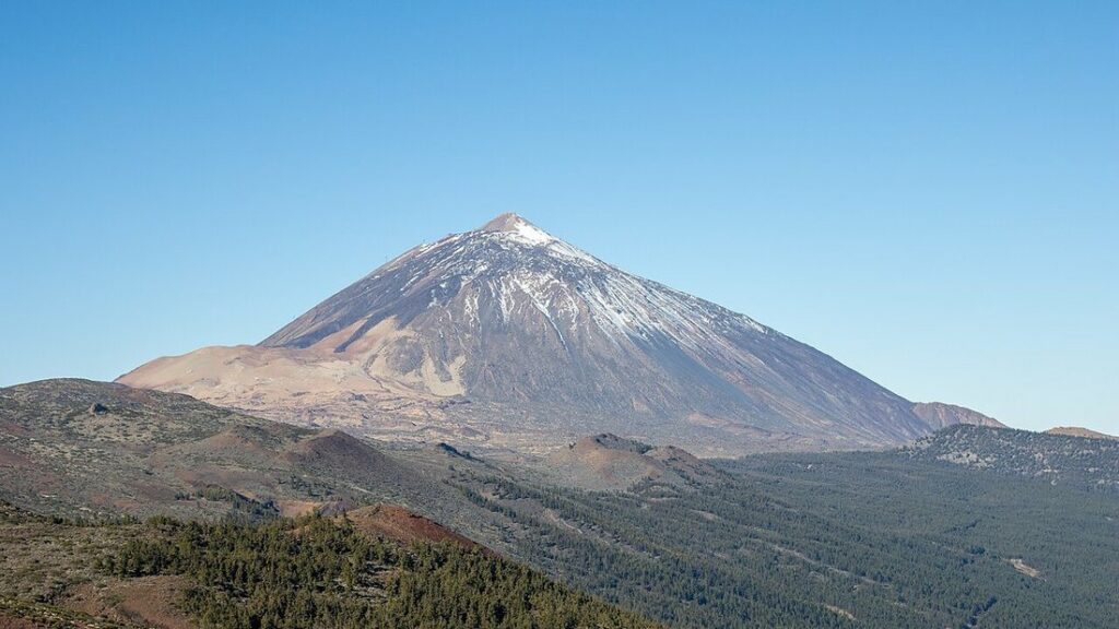 Le volcan Teide, sommet enneigé, au-dessus d'une forêt de pins et de pentes brunes, sous un ciel bleu