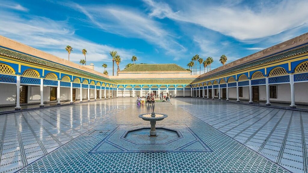 Grande cour carrelée de mosaïques, avec fontaine centrale, entourée de galeries à colonnes blanches et de palmiers