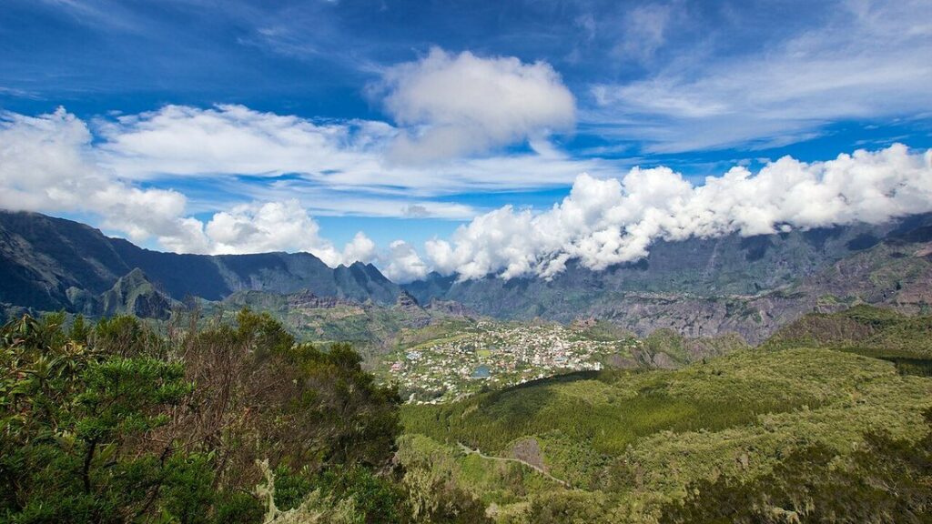 Ville au fond d'une cuvette entourée de hautes crêtes, avec des nuages blancs accrochés aux sommets, sous un ciel bleu