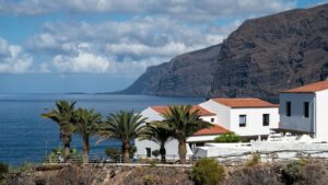 Palmiers et maisons blanches aux toits de tuiles rouges devant l'océan et les hautes falaises de Los Gigantes, à Tenerife