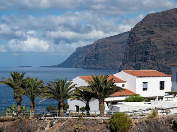 Palmiers et maisons blanches aux toits de tuiles rouges devant l'océan et les hautes falaises de Los Gigantes, à Tenerife