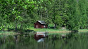 Petite cabane en rondins rouge au bord d'un lac entouré de bouleaux, avec une barque blanche amarrée