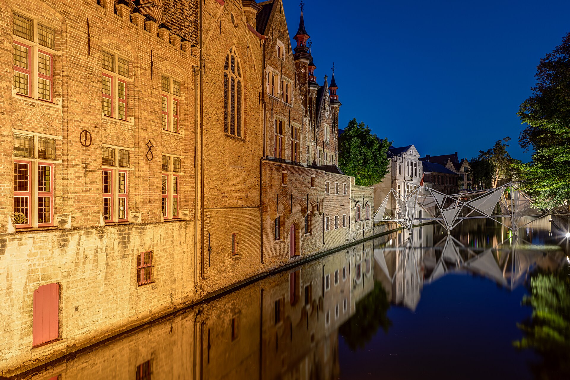 Façades de brique éclairées au crépuscule le long d'un canal, avec une passerelle métallique légère reflétée dans l'eau