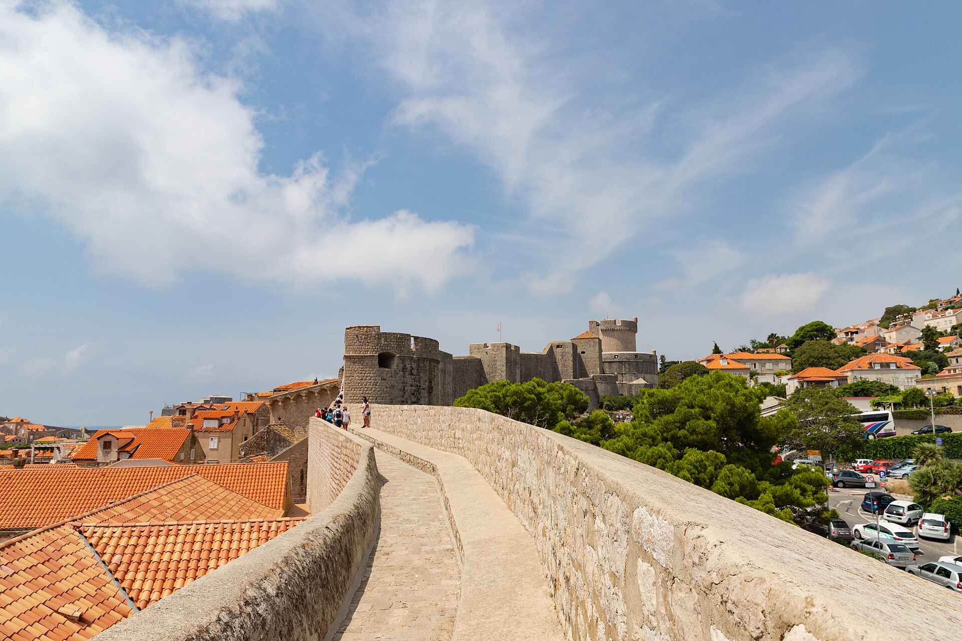 Chemin de ronde des remparts de Dubrovnik longeant des toits de tuiles orange, avec une grosse tour de pierre au fond