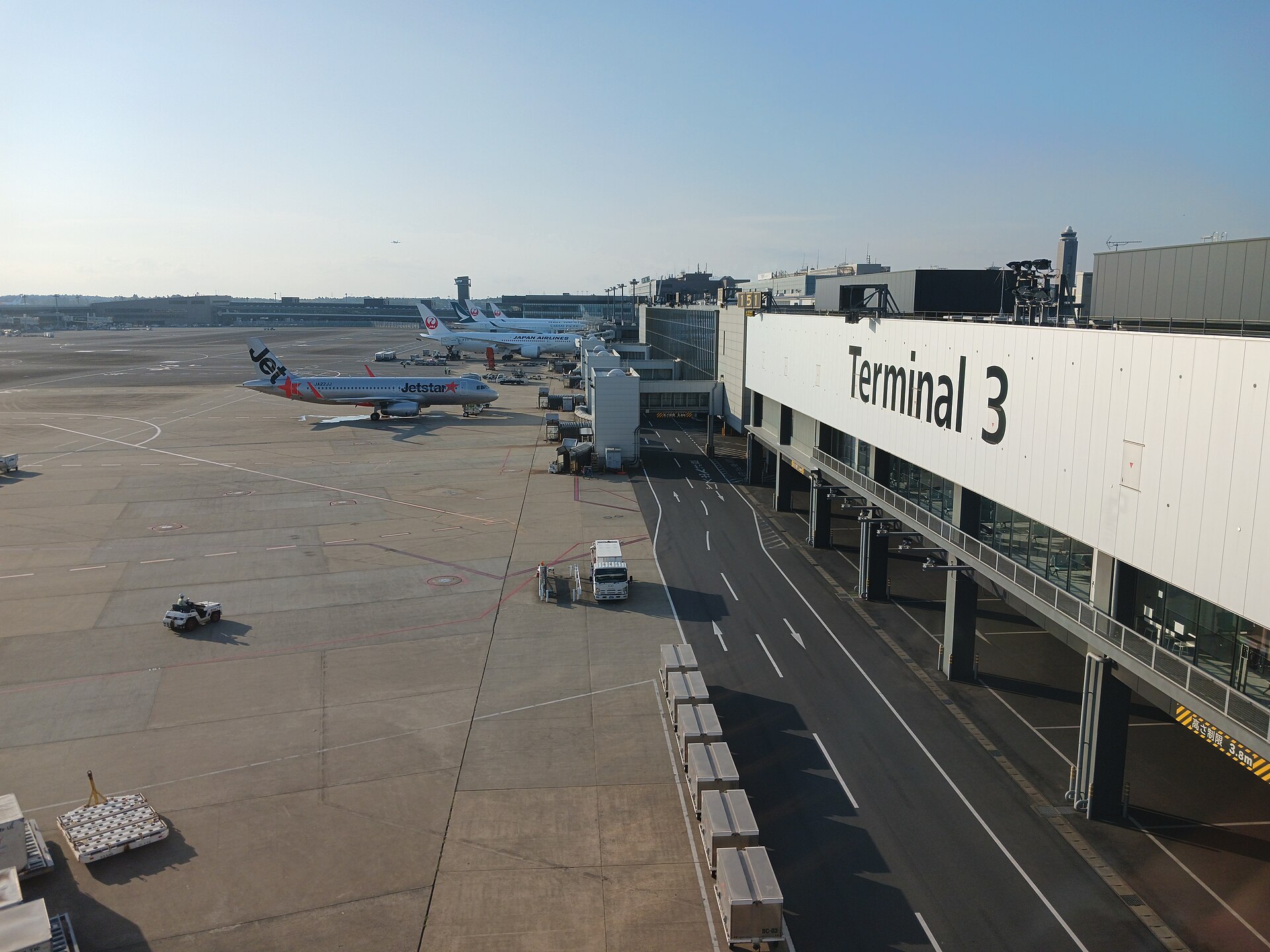 Façade blanche du terminal 3 d'un aéroport, avec un avion Jetstar et des appareils Japan Airlines sur le tarmac
