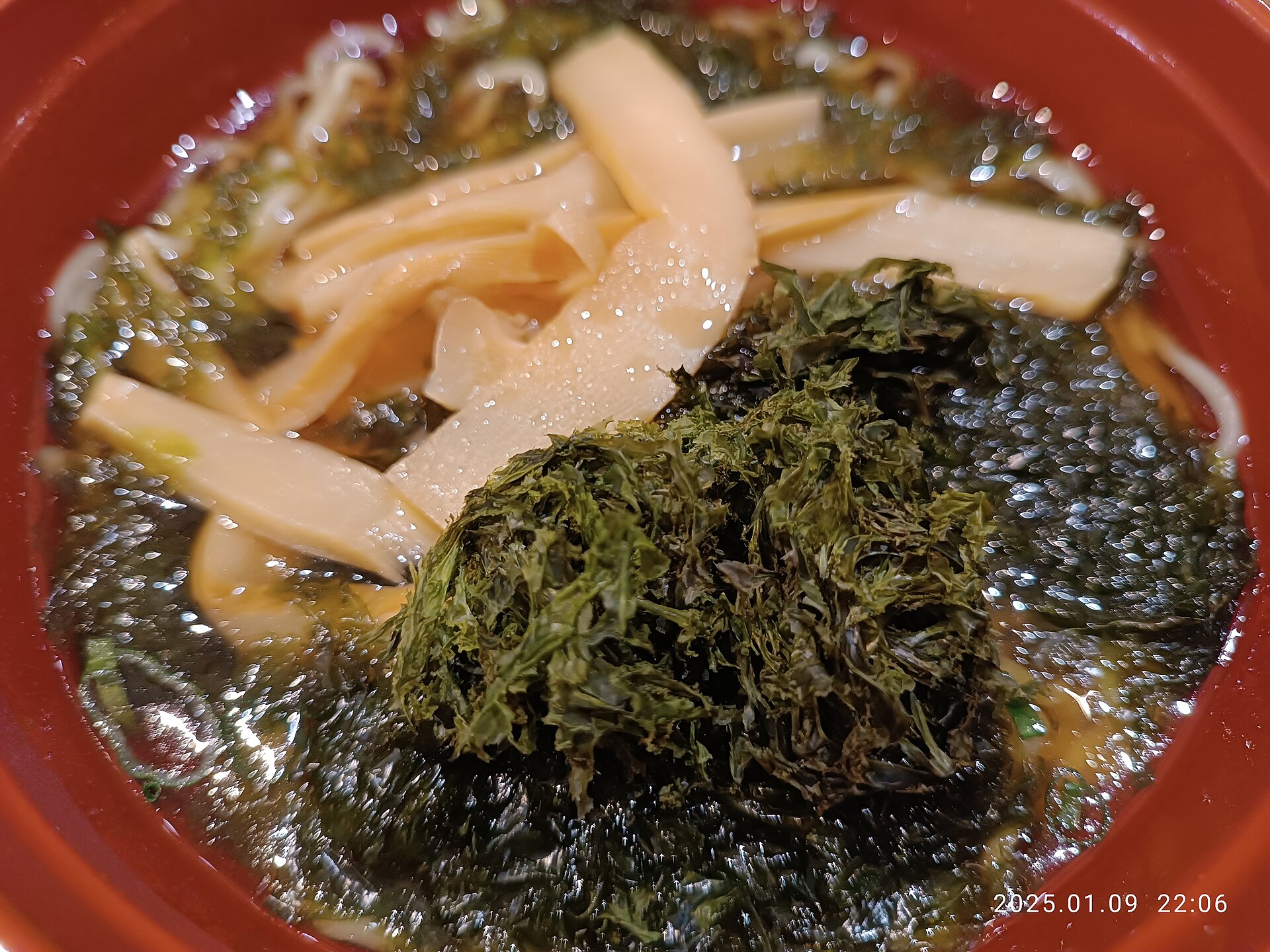 Bol rouge de soupe de nouilles garnie de feuilles d'algue nori, de lamelles de pousses de bambou et d'algues hachées
