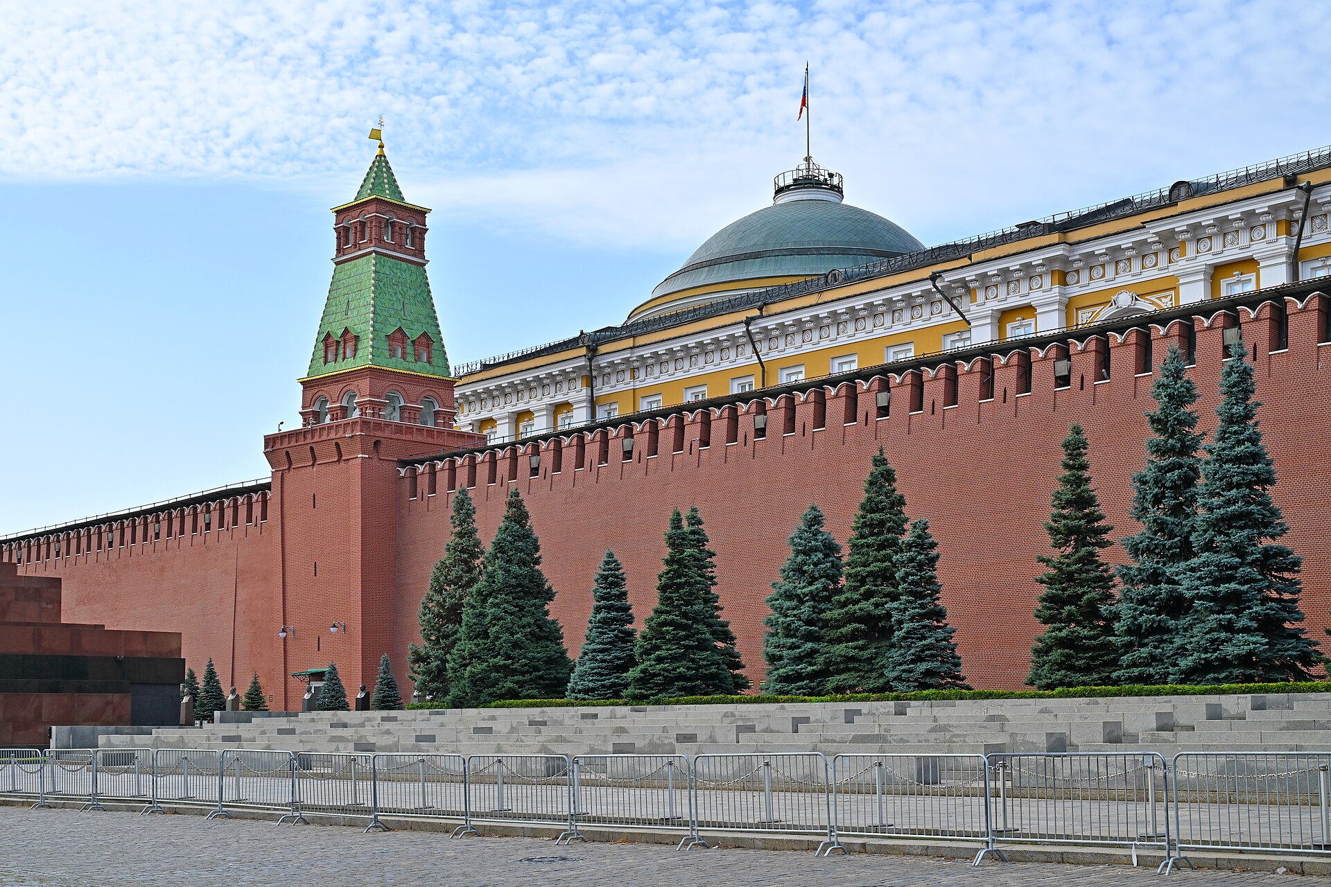 Muraille de brique rouge du Kremlin avec une tour à toit vert et un bâtiment jaune et blanc à dôme, vus de la place Rouge